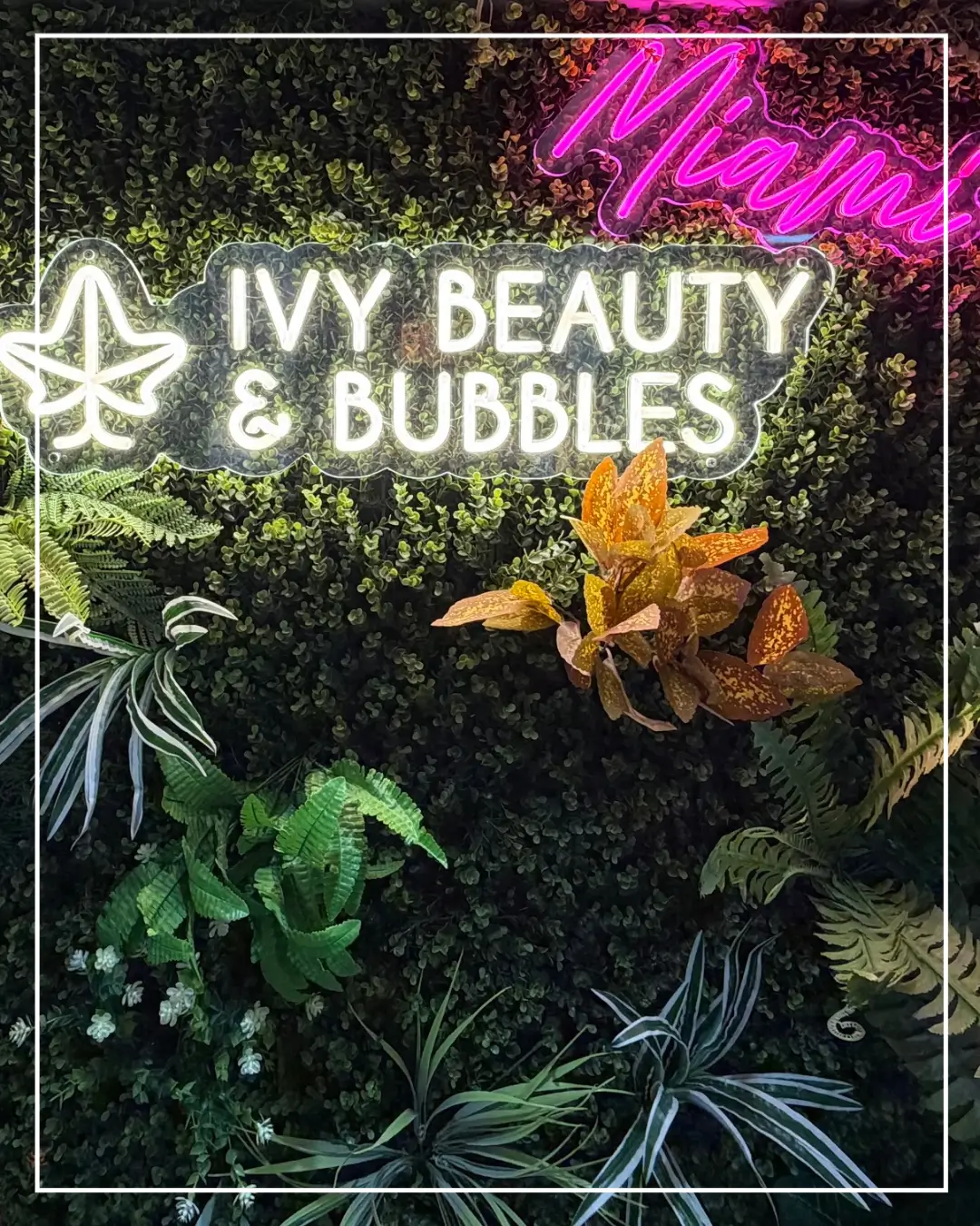 Plant wall with the illuminated IVY Beauty & Bubbles Abu Dhabi salon sign.